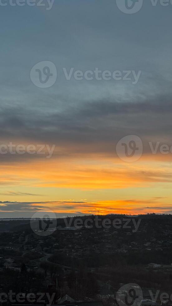 Dramatic sunset over a quiet town with vibrant sky and horizon silhouette in the evening with soft clouds illuminated by golden light photo