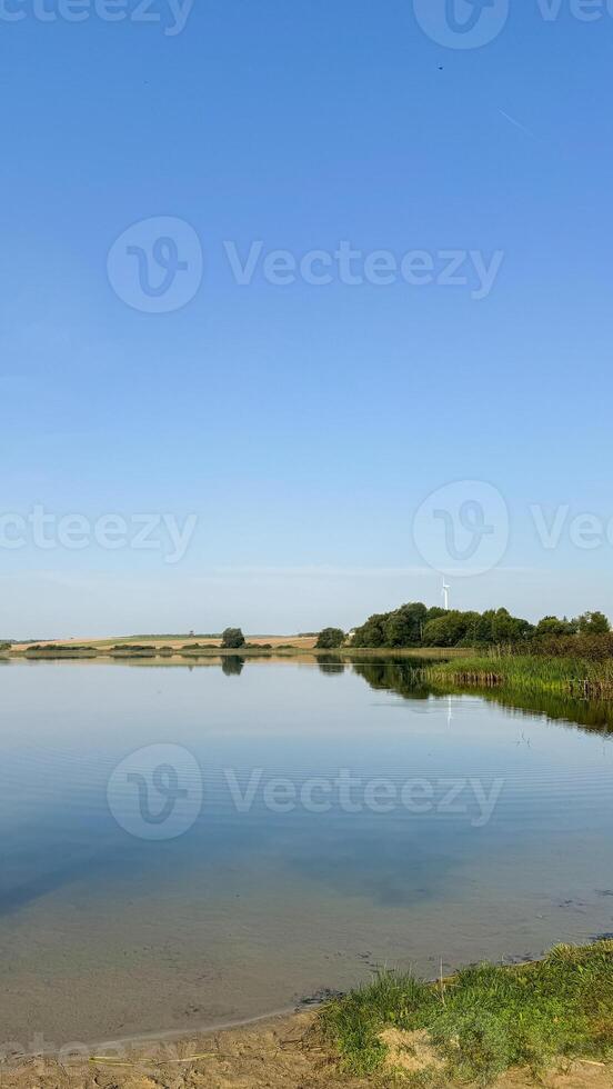 Serene lakeside landscape with clear blue sky and verdant greenery reflecting tranquility and natural beauty in a peaceful, scenic view photo