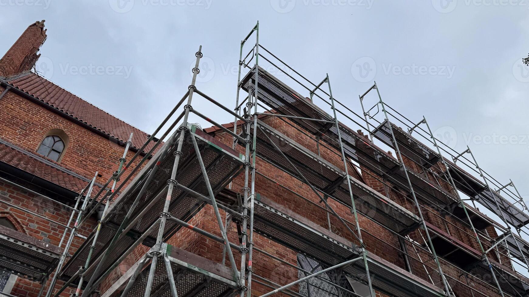 Scaffolding surrounds historic brick building under renovation against cloudy sky depicting construction process and architectural transformation photo