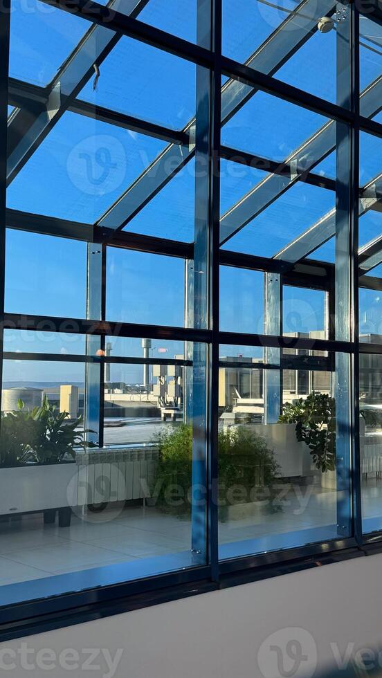 Sunlit modern greenhouse with tall blue framed glass walls and verdant potted plants on a clear sunny day offering scenic outdoor views photo