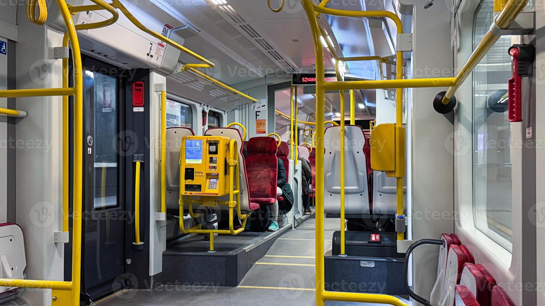 Modern urban train interior with yellow handrails and red seating on a daytime commute in a spacious and clean environment photo