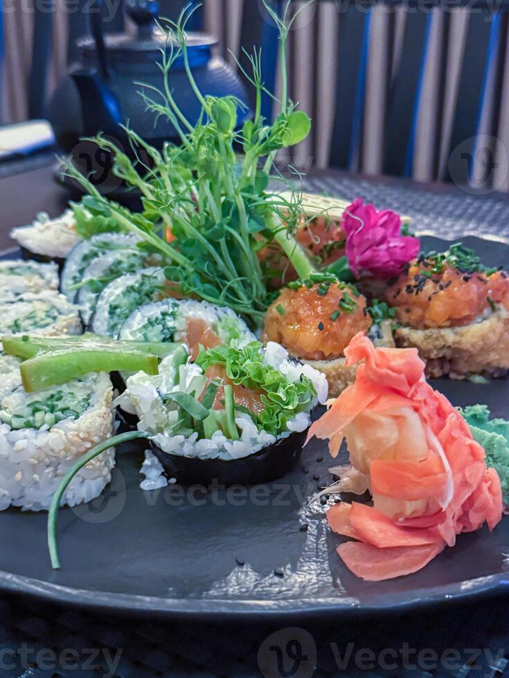 Vibrant sushi platter featuring fresh vegetables, rice rolls, and seaweed on a decorative grey plate with a background of tea set and wooden elements photo