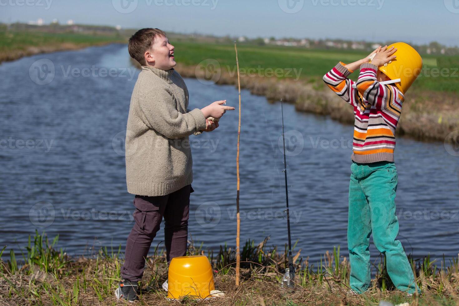 Two boys are fishing and having fun. One of them put a bucket on his head. photo