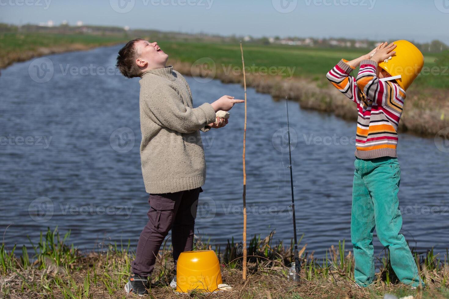 Two boys are fishing and having fun. One of them put a bucket on his head photo