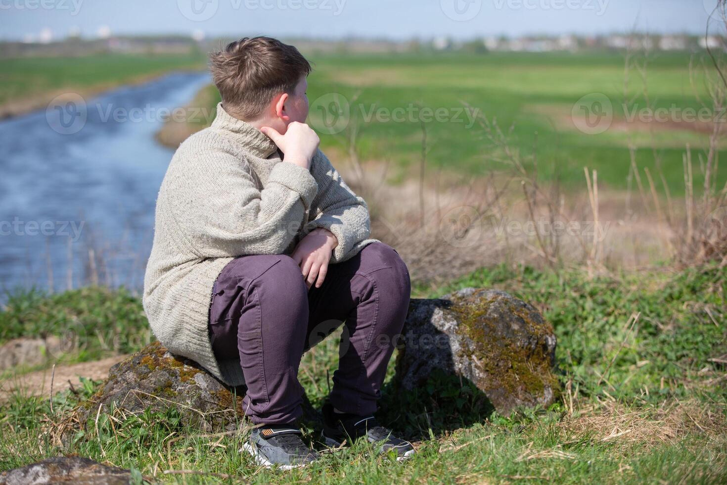 A chubby, plump teenage boy of twelve years old sits against the backdrop of nature and is sad. photo