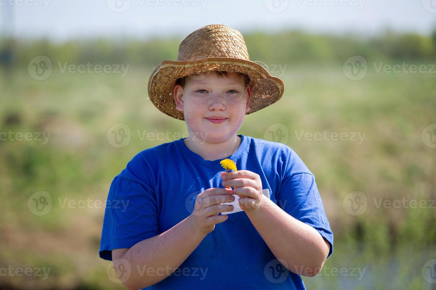 Portrait of a funny teenage boy in a straw hat against the backdrop of summer nature. A freckled boy in the summer. photo