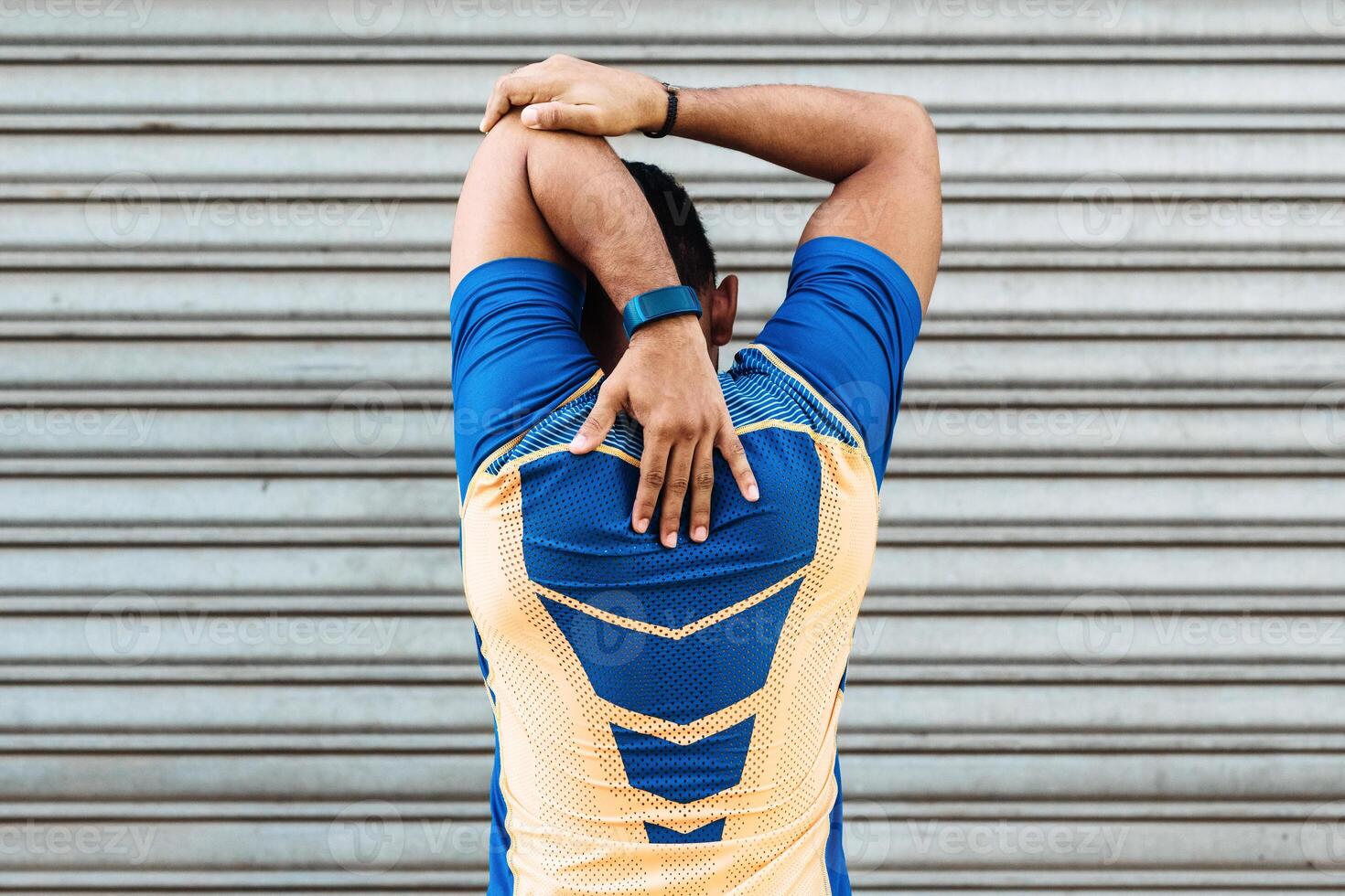 Back view of a young hispanic male doing arm exercises in front of a garage door photo