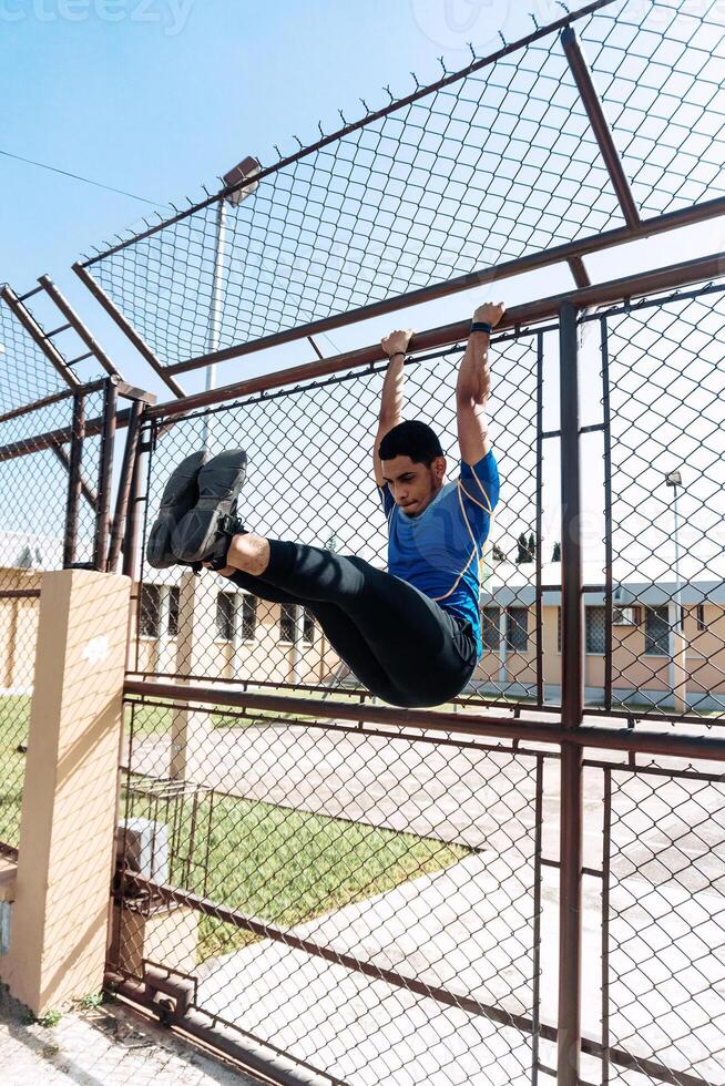 Portrait of Young hispanic male exercising abs hanging on a grid fence photo
