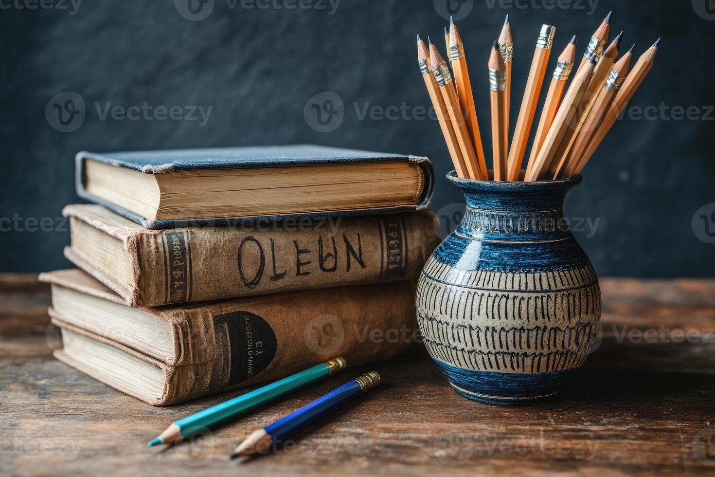 Pencils in vase next to stack of old books on desk photo
