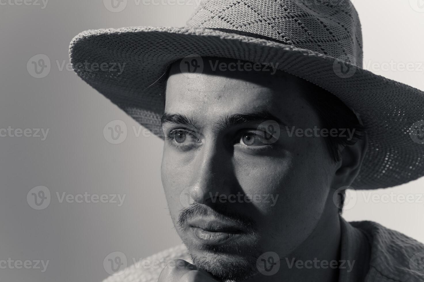 Captivating portrait of a young man in a woven hat, showcasing deep contemplation and artistic expression in soft light photo