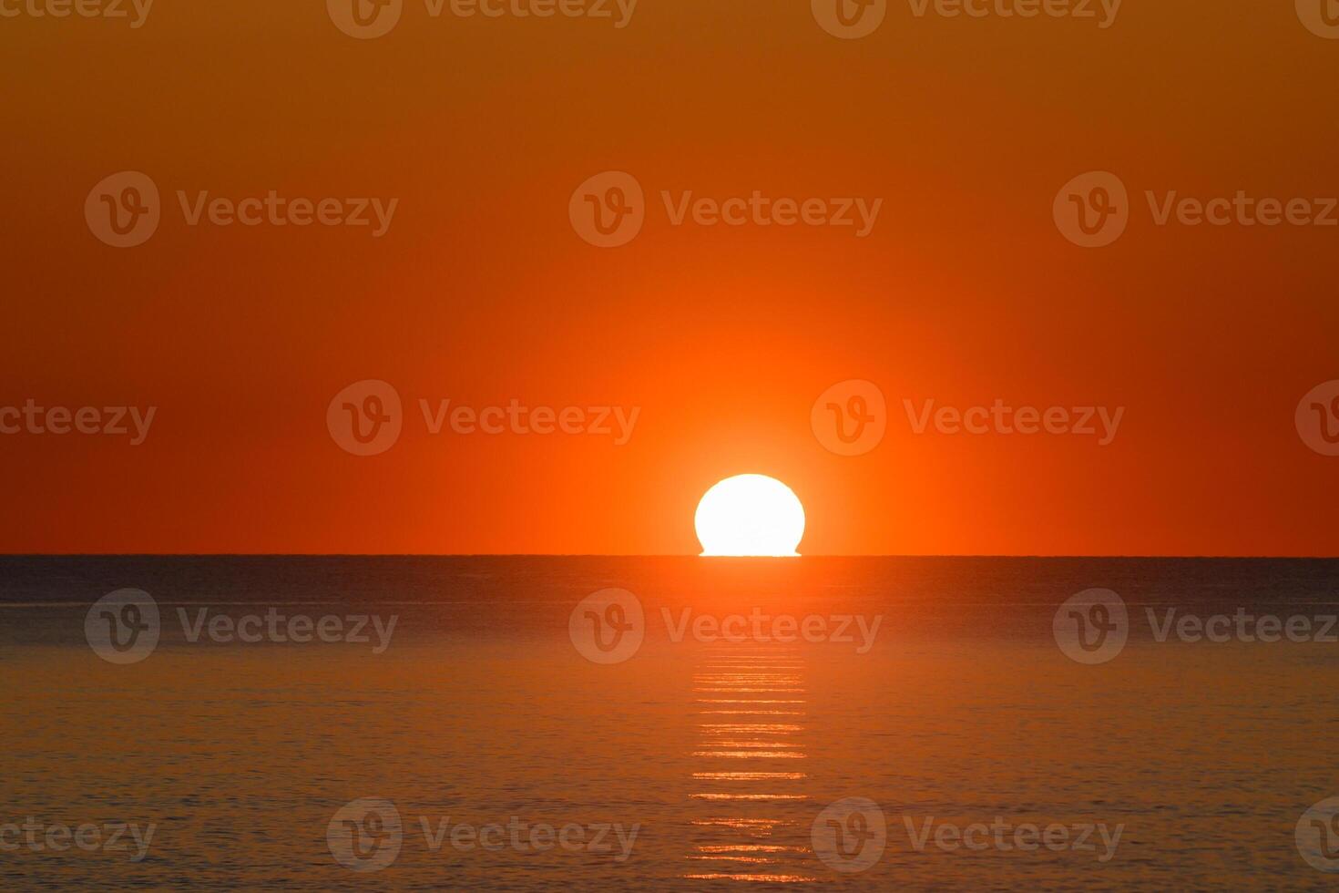 Vibrant sunset paints the sky and water with shades of orange and gold over the calm ocean horizon photo