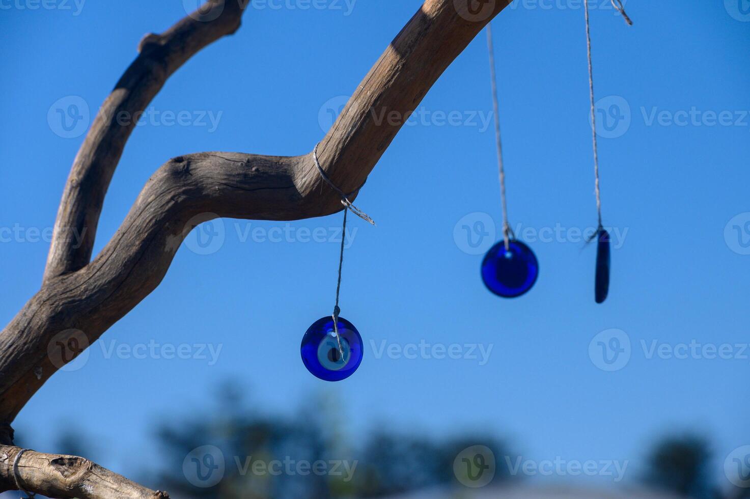 Vibrant blue glass ornaments dangle gracefully from a bare wooden branch under a clear autumn sky photo
