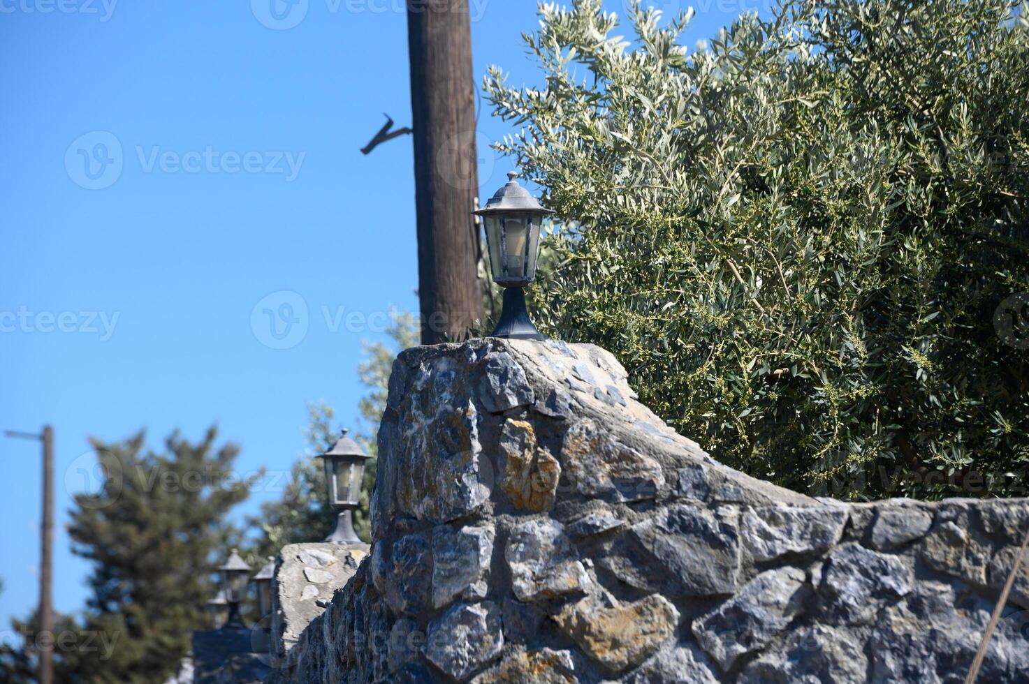 Charming stone wall with vintage lanterns under a clear blue sky in a serene countryside setting at midday photo