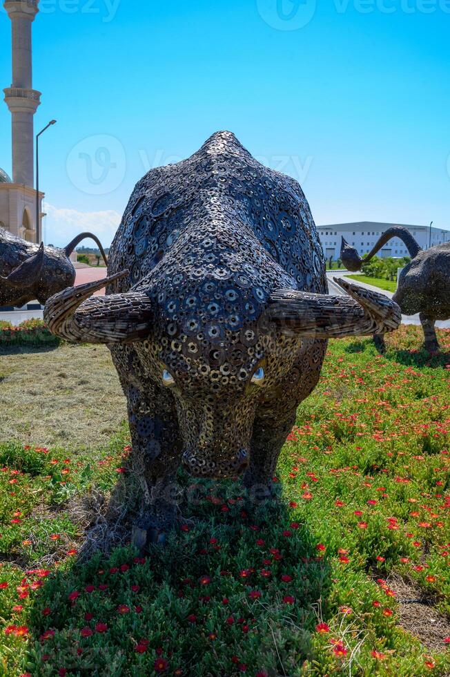 Sculptures of metal bulls standing on green grass with the main mosque and minaret in the background. Cultural and symbolic scene. photo