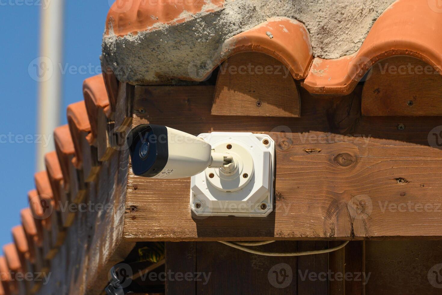 Surveillance camera monitoring a rustic building under clear blue skies in a sunny environment photo