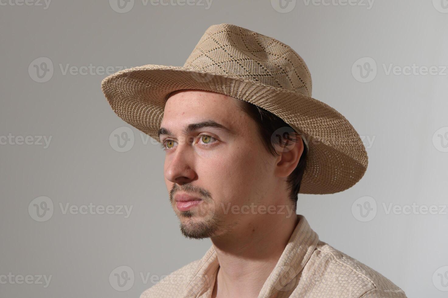 Young man with a straw hat gazes thoughtfully, reflecting on his surroundings in a serene indoor setting photo