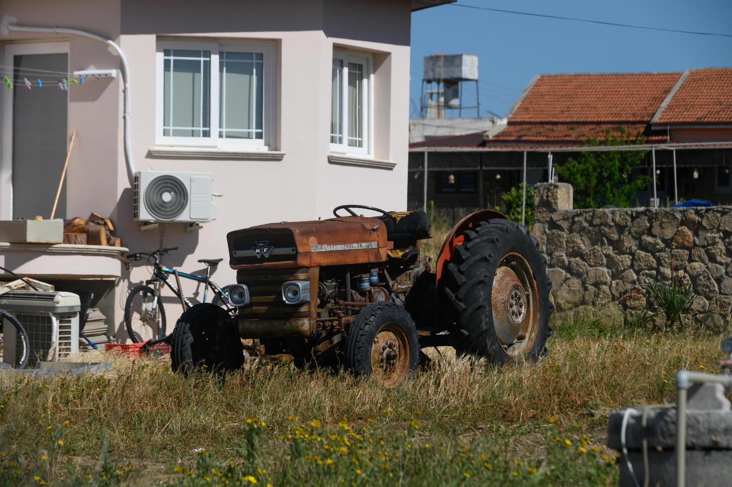 Gaziveren Cyprus -15.04.2025 Old tractor rests beside a quaint house, surrounded by lush grass and a serene, rural landscape in warm daylight photo
