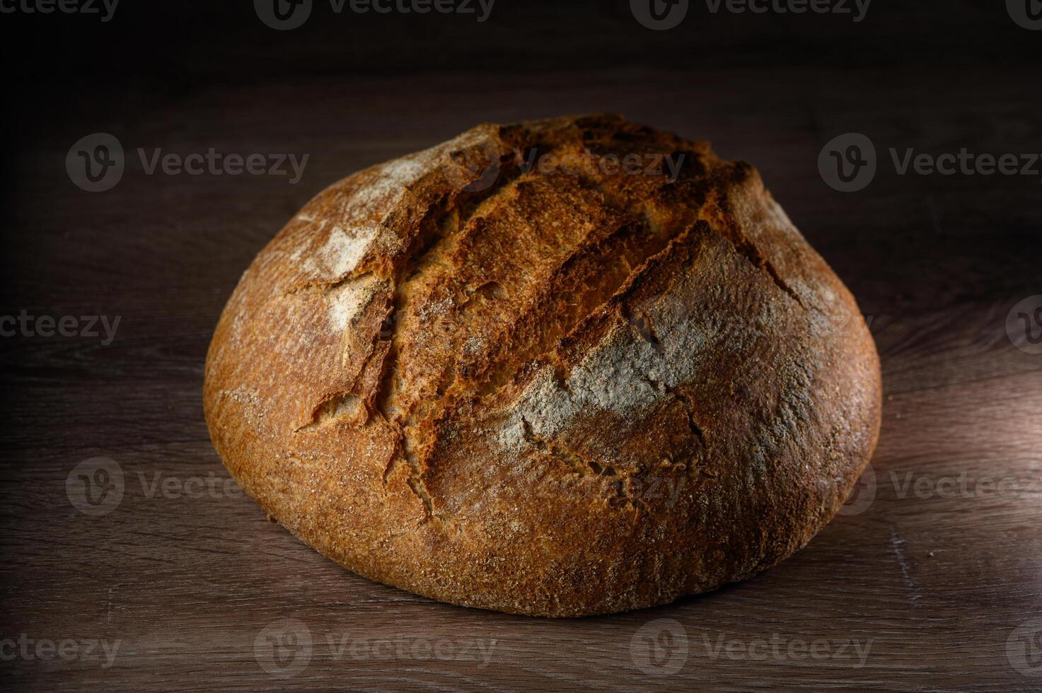 Artisan bread loaf resting on wooden surface with warm light highlighting crust photo