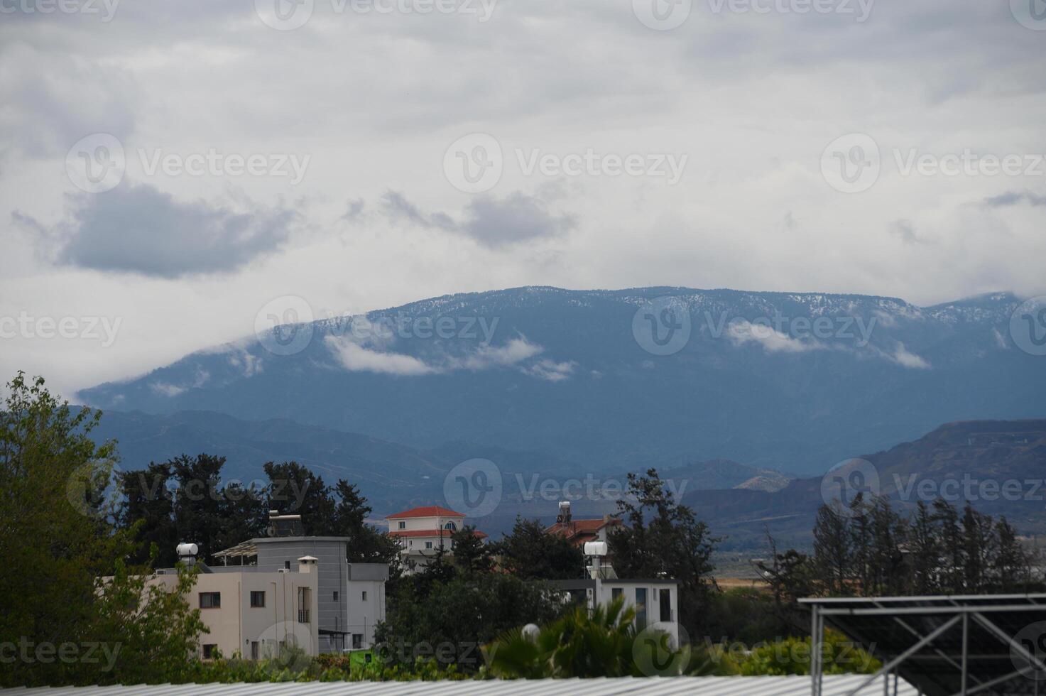 Cloudy mountain landscape with snow-capped peaks and distant buildings under a moody sky photo