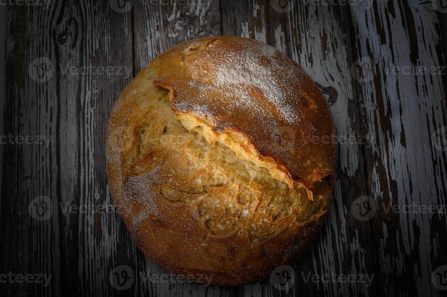 Freshly baked round loaf resting on rustic wooden table with a golden crust photo