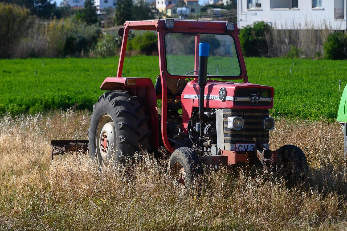 Gaziveren Cyprus -10.04.2025 Old red tractor resting among golden grass in a vibrant green field under a clear blue sky during a sunny afternoon photo
