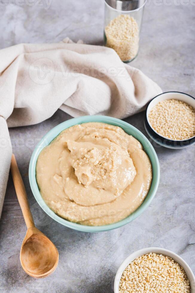 Homemade sesame tahini in bowl on grey table vertical view photo