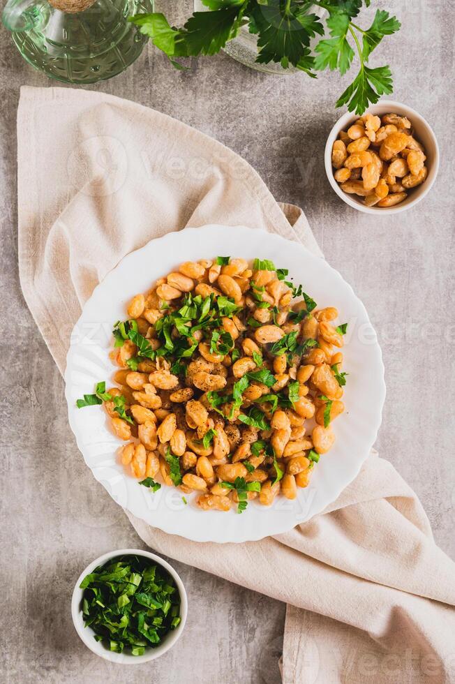 Homemade fried white beans and greens salad on plate on table top and vertical view photo