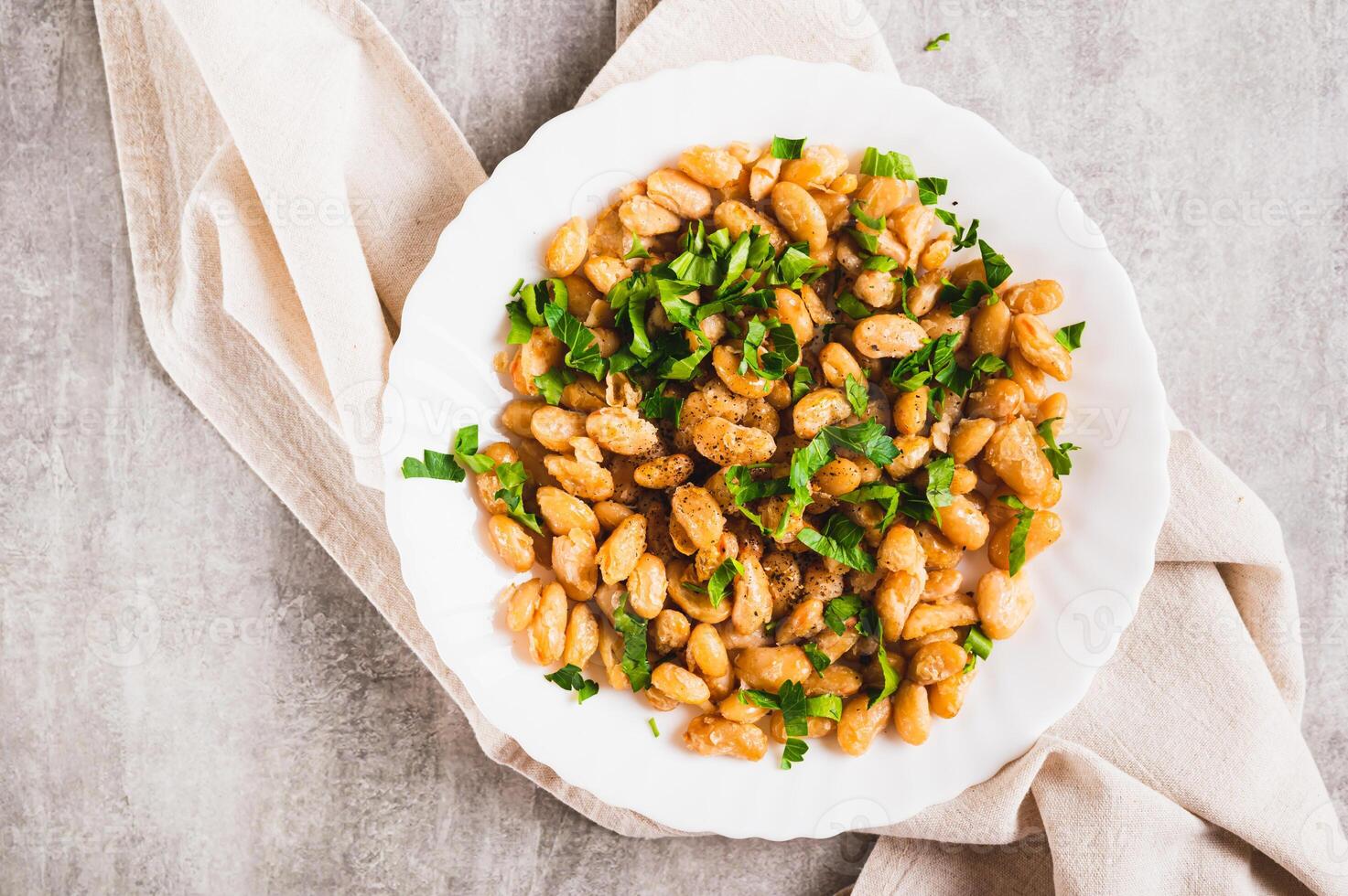 Close up of warm salad of white fried beans and parsley on a plate on the table top view photo