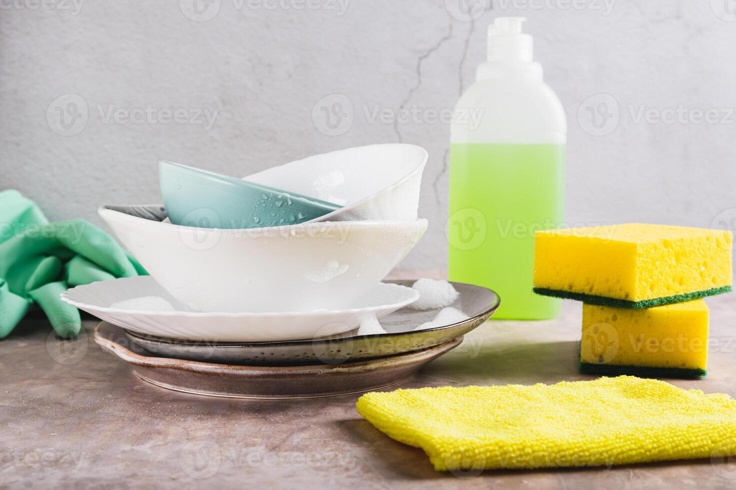 Stack of plates in foam, cloth, sponges, gloves and detergent on table photo