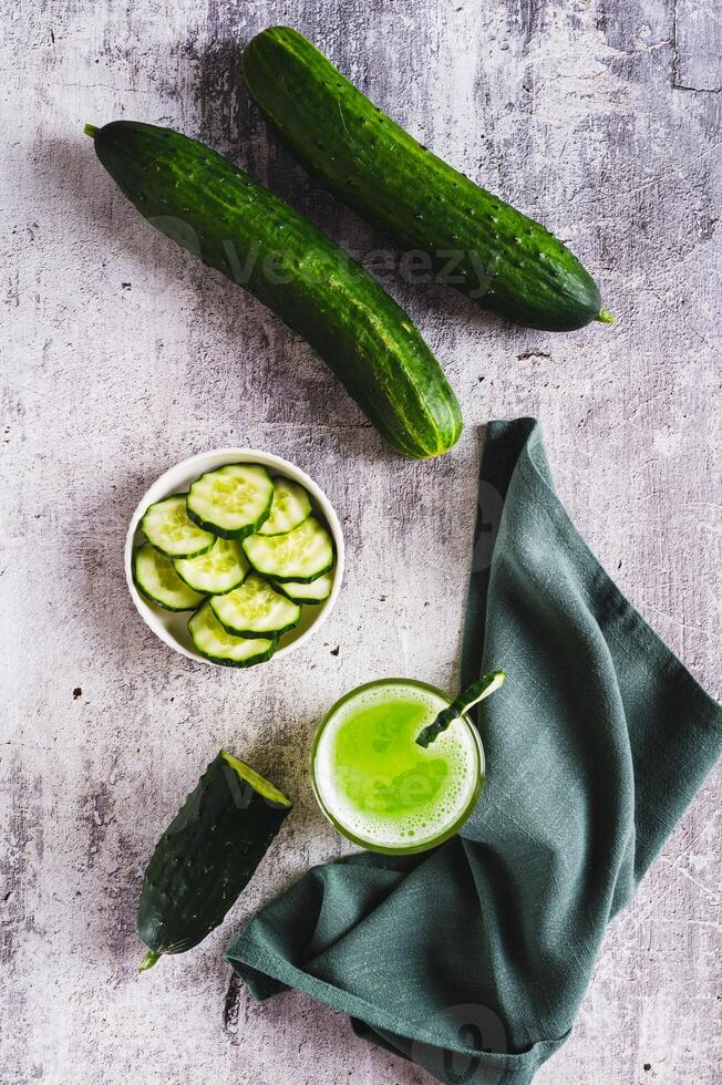 A glass of fresh cucumber juice and cucumbers on the table top and vertical view photo