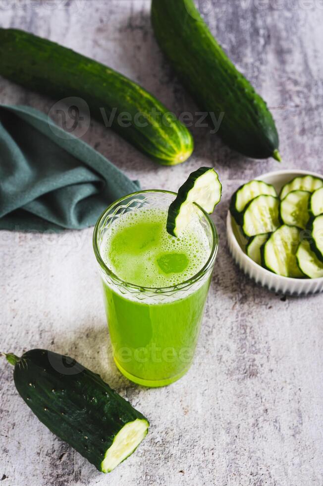 A glass of fresh cucumber juice and cucumbers on the table vertical view photo