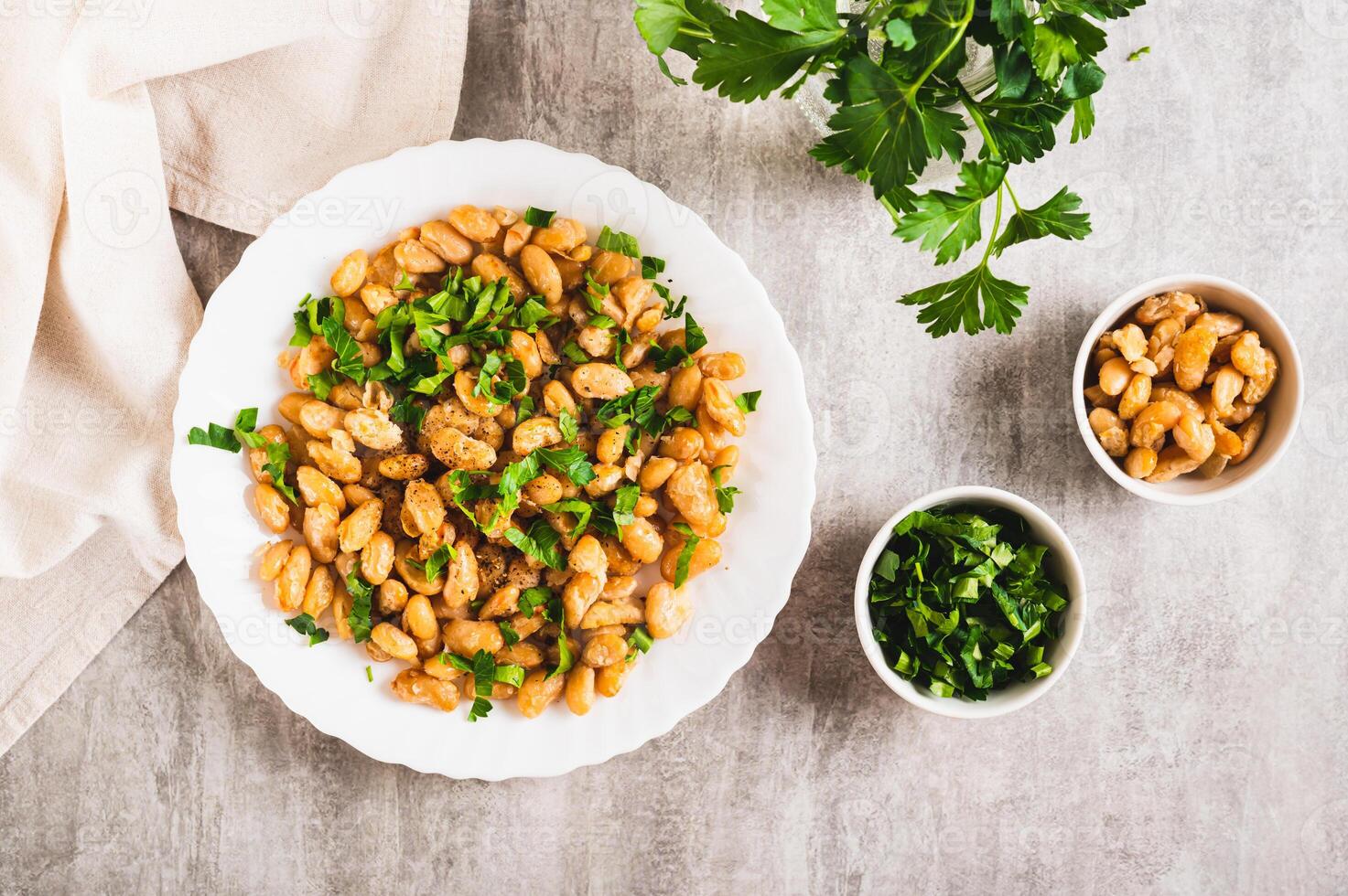 Warm salad of white fried beans and parsley on a plate on the table top view photo