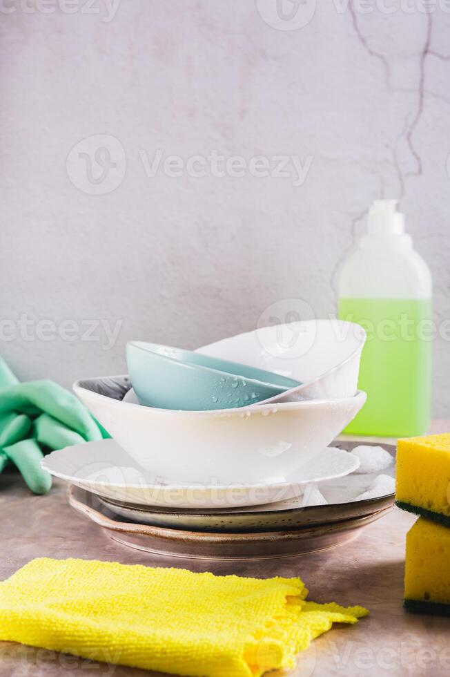 Stack of plates in foam, cloth, sponges, gloves and detergent on table vertical view photo