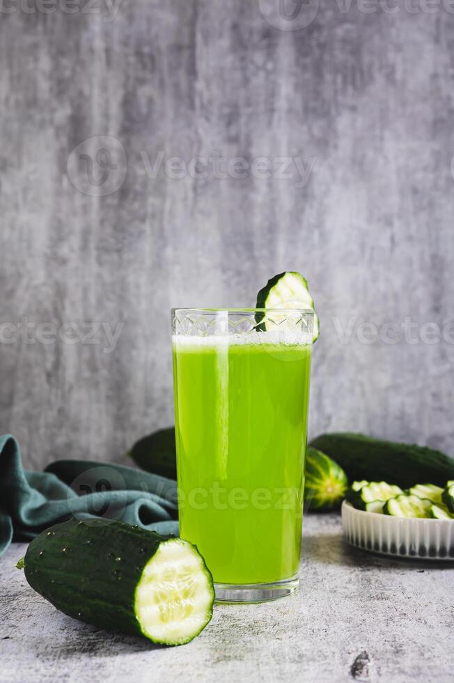 Fresh cucumber juice in a glass and cucumber pieces in a bowl on the table vertical view photo