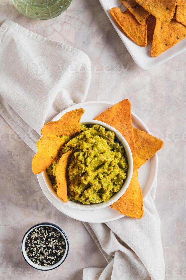 Delicious guacamole in a bowl and tortilla chips on a plate on the table top and vertical view photo