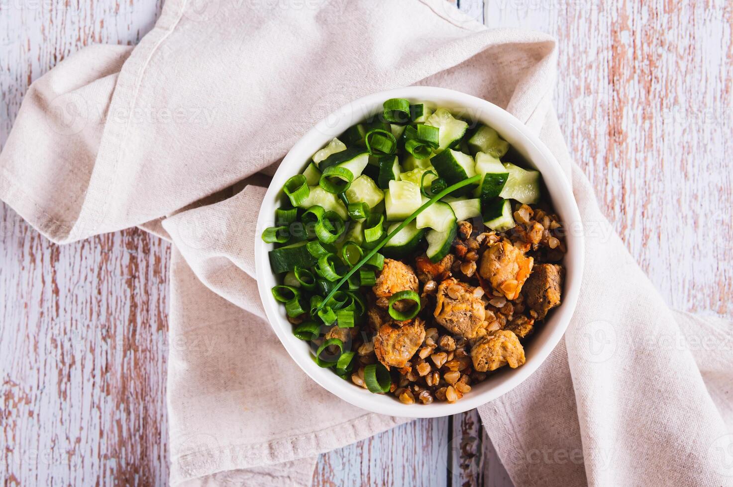 Close up of buckwheat porridge with meat, cucumber and chives in a bowl on the table top view photo