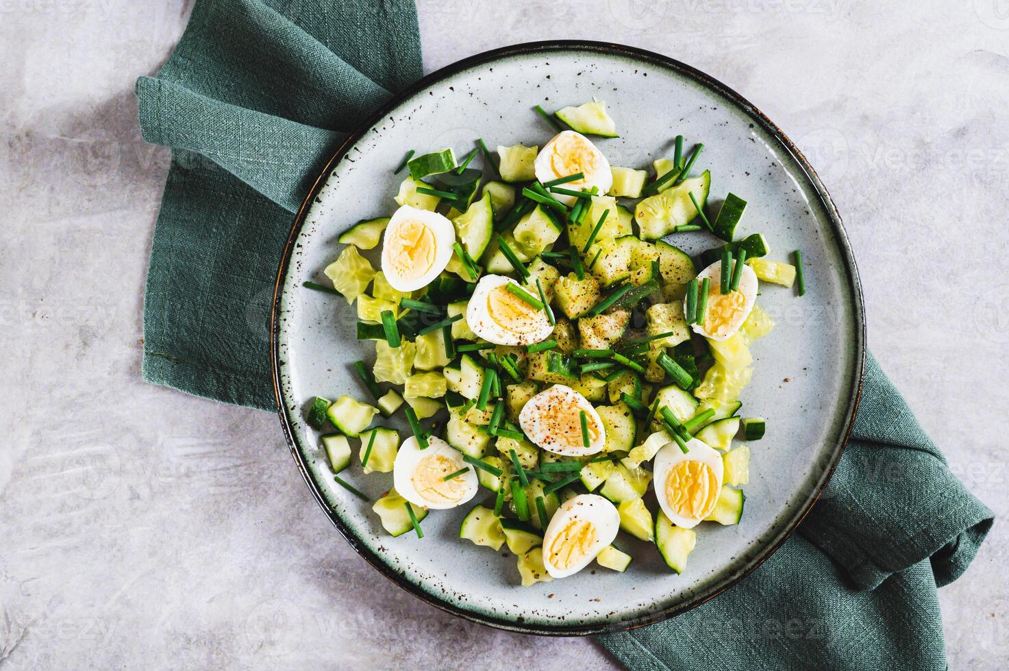 Close up of fresh salad of cucumbers, quail eggs and green onions on a plate top view photo