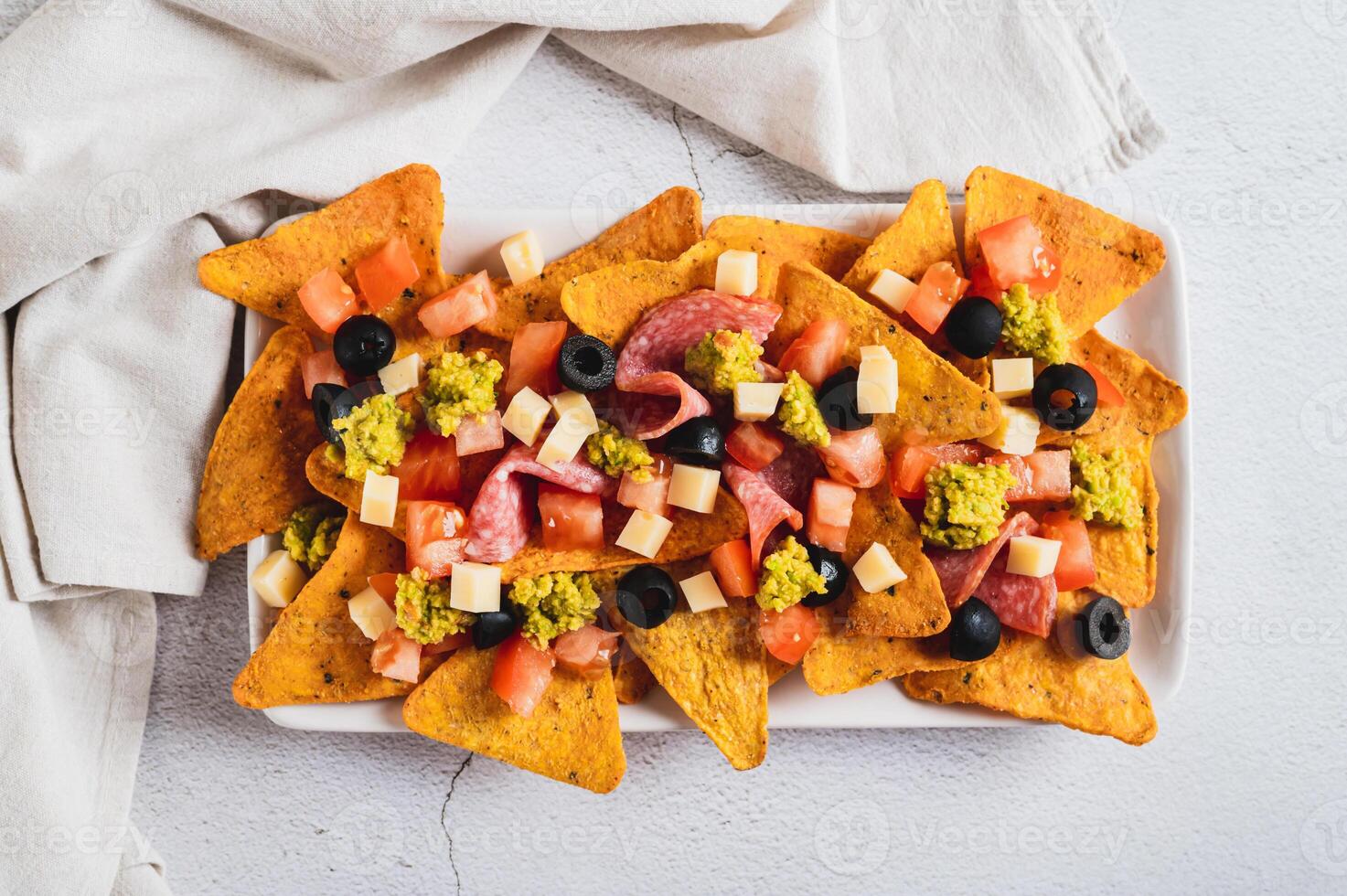 Close up of mexican nachos chips with olives, tomatoes, salami and cheese on a plate top view photo