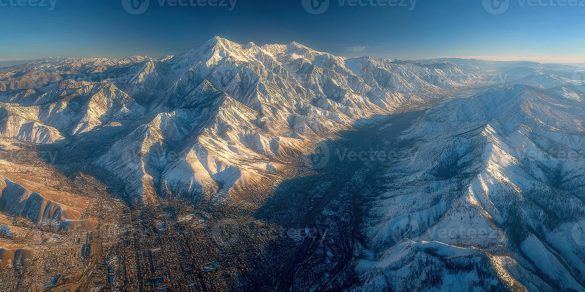 Snow-covered mountains tower over a valley near a city during golden hour in the early evening photo