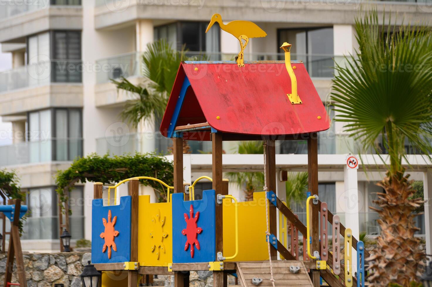 Brightly colored playground structure under a cloudy sky near a coastal setting with vibrant palms in full view photo