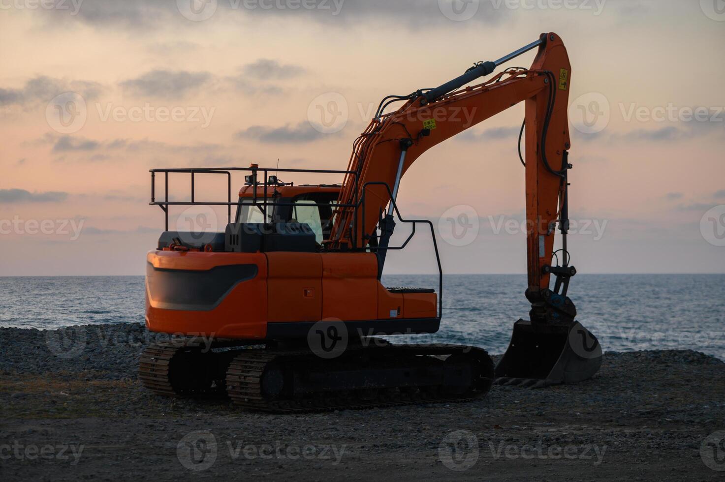 Excavator poised for work at the shoreline during a tranquil sunset over the ocean photo