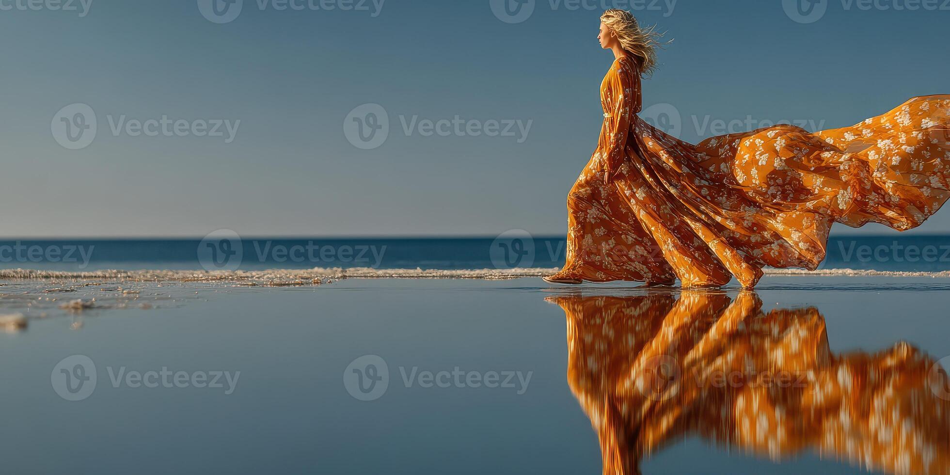 Woman walks gracefully along the beach in a flowing orange dress at sunset near calm waters reflecting the sky photo