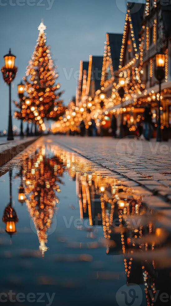 Holiday lights reflect on a cobblestone street beside an illuminated Christmas tree at dusk in a festive town square photo