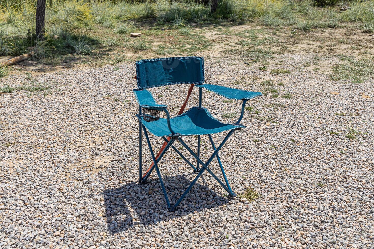 Horizontal photo of green landscape with camping chair and gravel path on sunny day