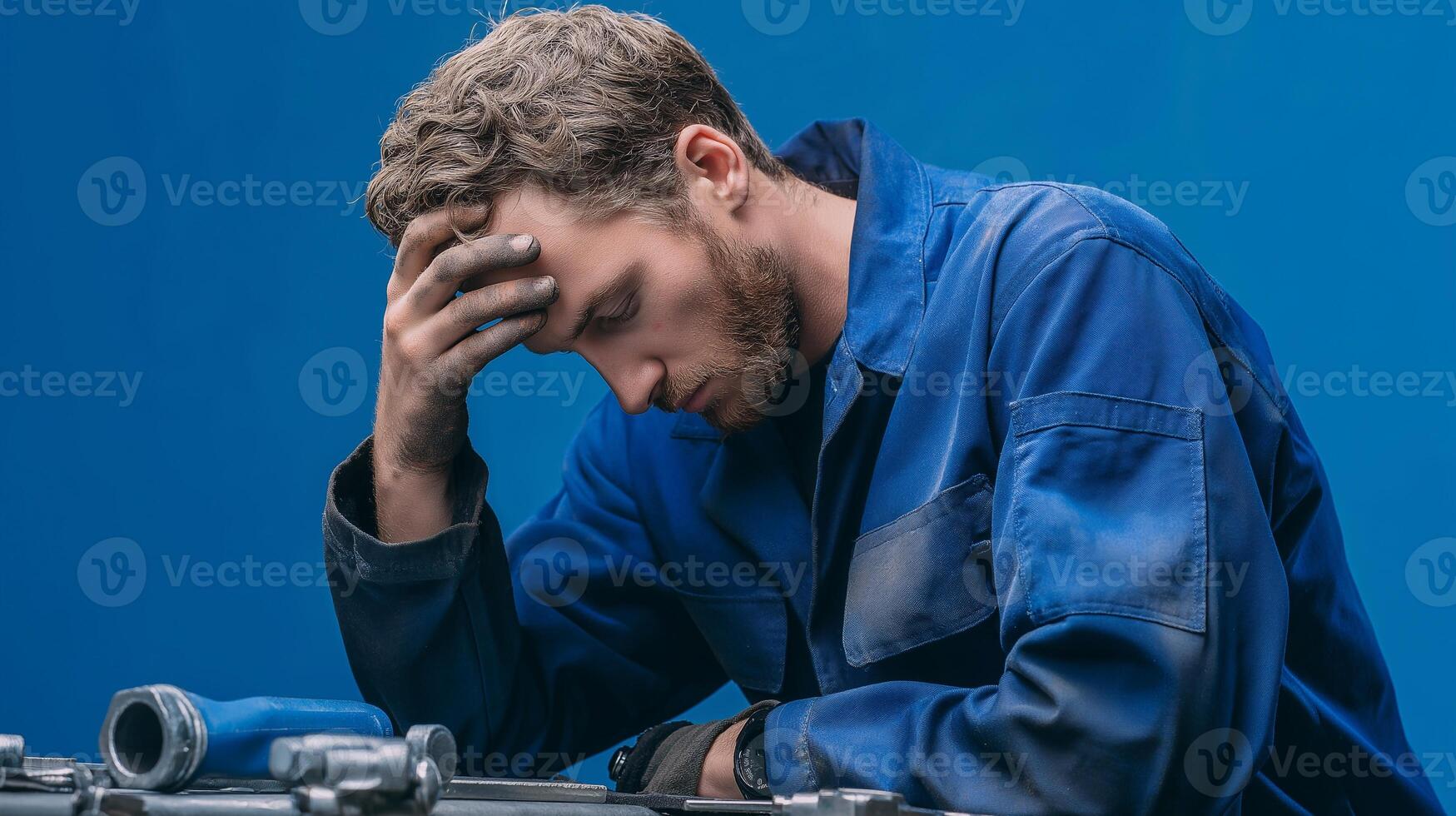 Stressed man in blue uniform showing signs of fatigue and burnout, holding head in frustration, studio portrait on neutral background, emotional expression of exhaustion. photo