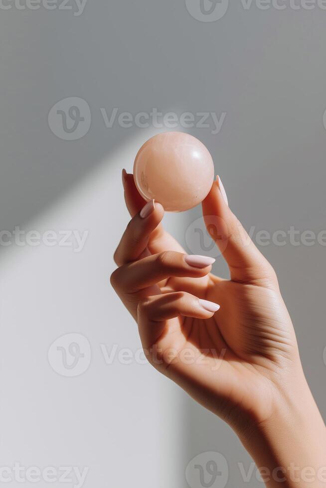 Hand holding a smooth pink crystal sphere against a soft gradient background, showcasing the delicate texture and natural beauty of the stone, emphasizing wellness and mindfulness concepts photo