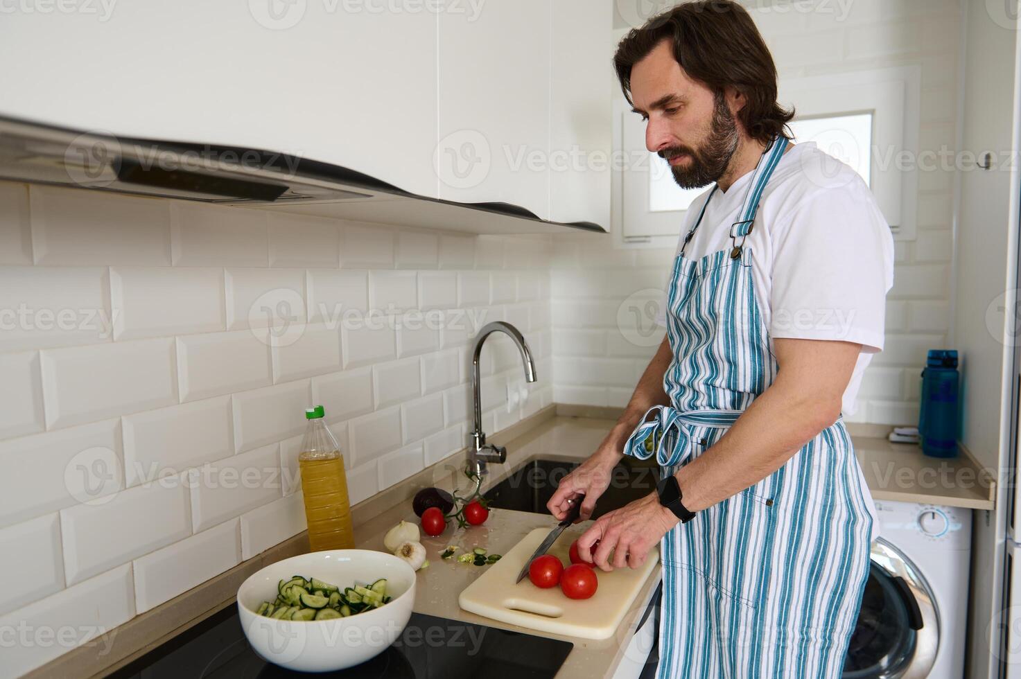 Man Preparing Fresh Salad in a Modern Kitchen Wearing Striped Apron photo