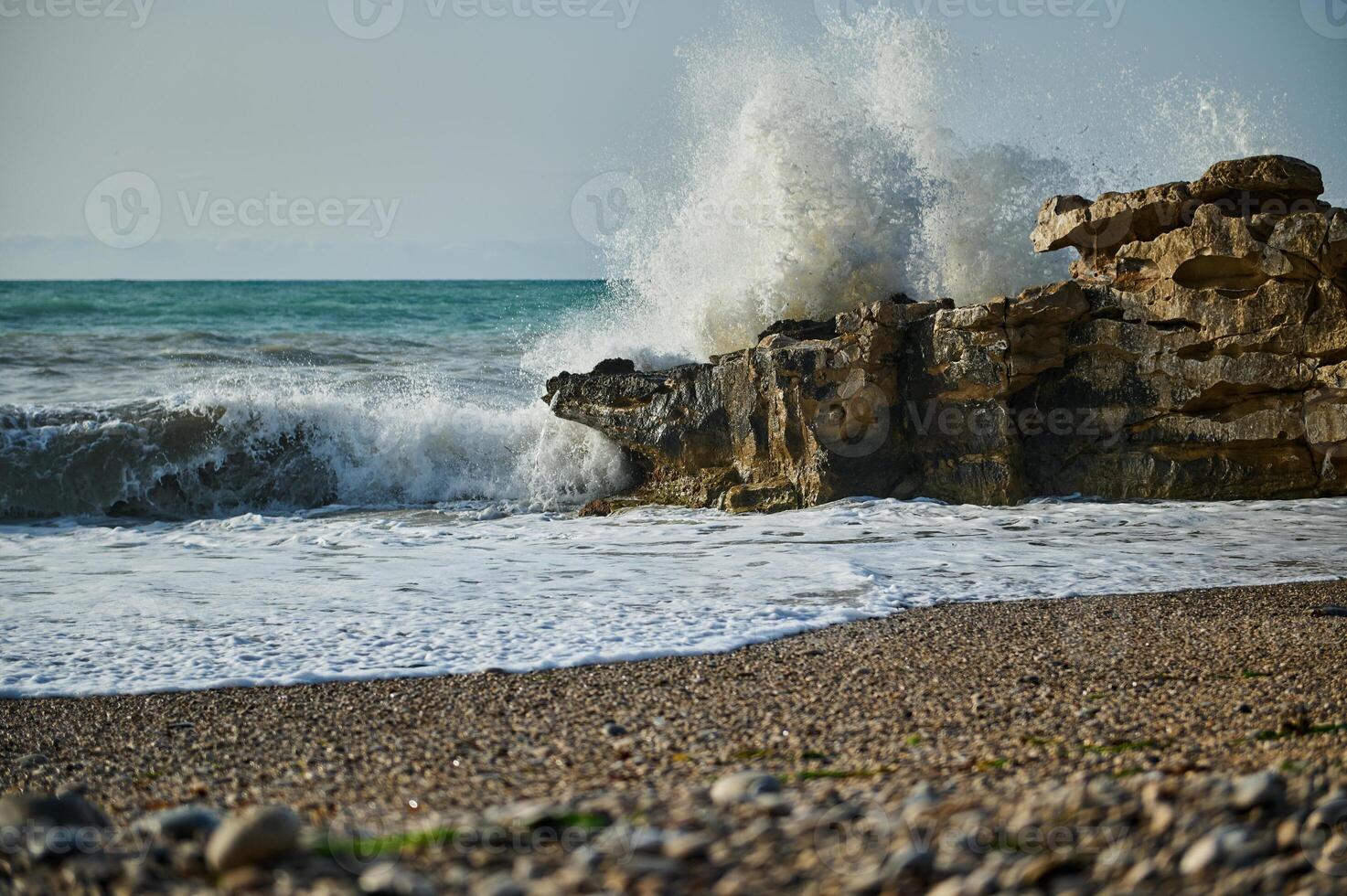 Large Ocean Wave Crashing Against Coastal Rock Formation on a Pebble Beach photo