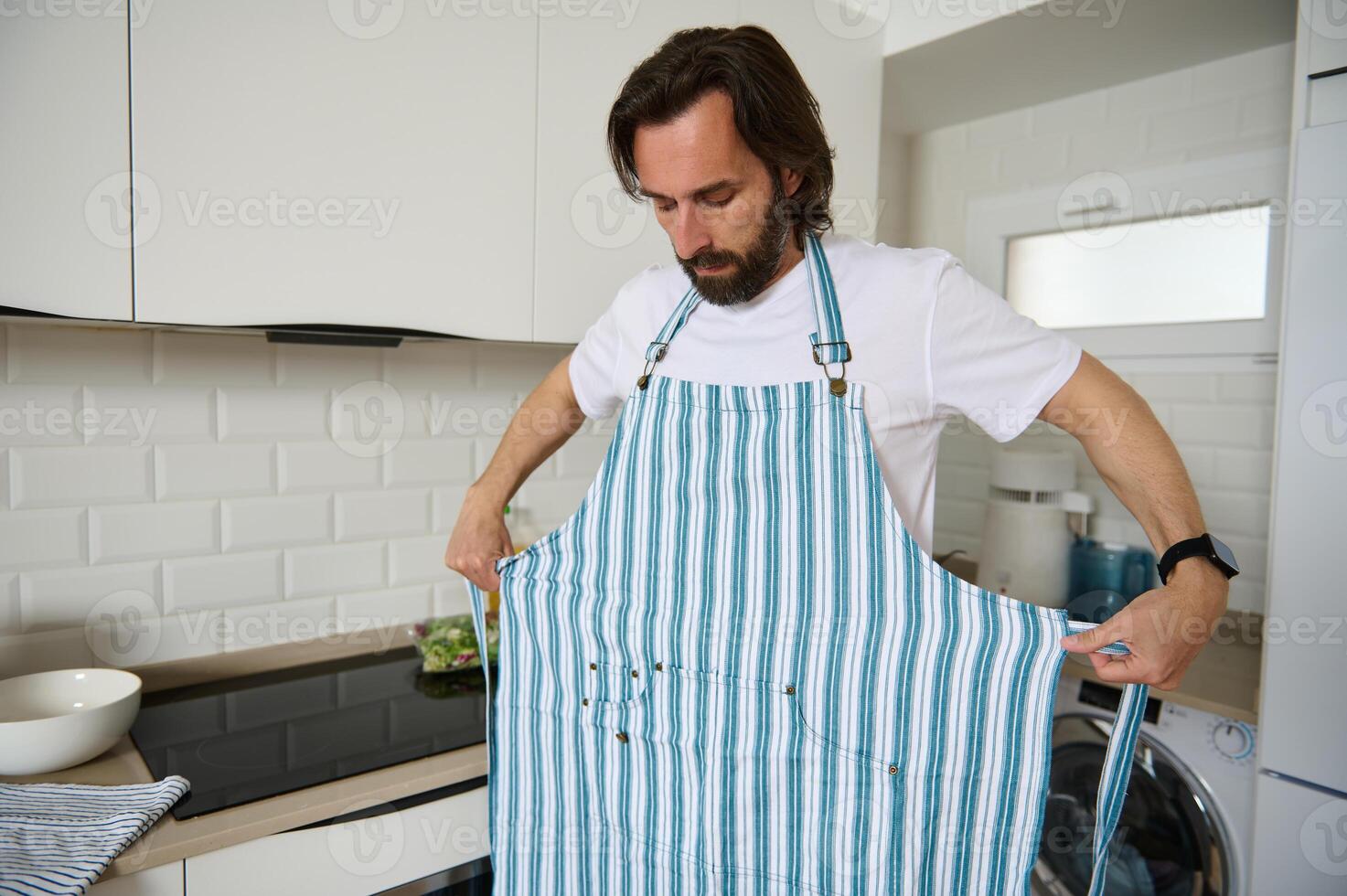 Man in Kitchen Adjusting Apron Preparing to Cook a Meal photo