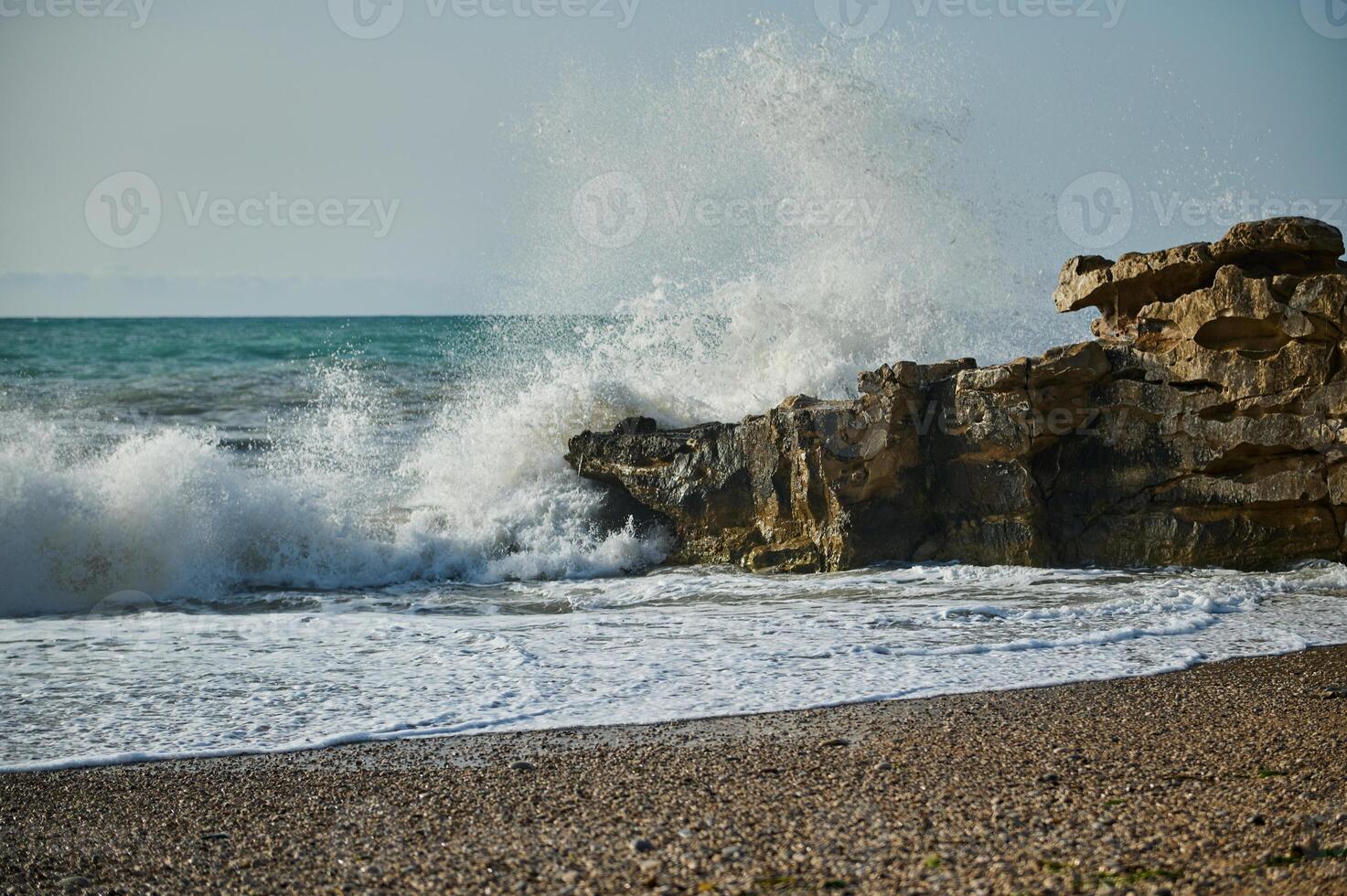 Serene Ocean Waves Crashing Against Coastal Rock Formations on a Pebbled Beach photo